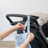 A person attaches a Bumkins Wet/Dry Clutch: Mickey + Minnie Sunny Side Up to a stroller handle indoors.
