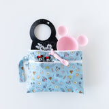 Bumkins Wet/Dry Clutch: Mickey + Minnie Sunny Side Up holds a black bib, pink plate, spoon, and two figures on a white background.