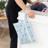 A person leans by a baby on a changing table with a bag from Bumkins On-The-Go Mealtime 5-Piece Set: Mickey + Minnie Mouse Sunny Side Up Pink.