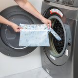 A person holds the Bumkins Wet/Dry Clutch: Mickey + Minnie Sunny Side Up in front of a front-loading washing machine.