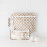 Bumkins Wet Bag + Clear Travel Bag 3 Pack Set in Sand Check—stylish travel organization, shown against a white brick wall.