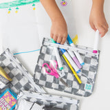 A child removes markers from a Bumkins Clear Travel Bag 3 Pack: Charcoal Check at a white table.
