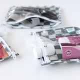 Close-up of Bumkins Clear Travel Bag 3 Pack: Charcoal Check with toiletries on a white background.