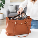 A person places a Roamio by Bumkins Clear Travel Bag 3 Pack: Leopard in a brown purse on a white table.