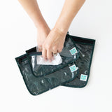 A person uses a wipe to clean the inside of Bumkins Clear Travel Bag 3 Pack: Starry Cactus on a white table.