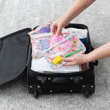 Someone packs Bumkins Packing Cube 2 Pack + Clear Travel Bag 3 Pack Set: Boots into an open suitcase on a light carpeted floor.