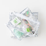 Roamio by Bumkins Clear Travel Bag 3 Pack: Disco Check is stacked on a white background, with glasses, a contact lens case, & toiletries.