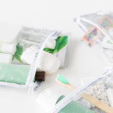 Close-up of toiletries in Roamio by Bumkins Clear Travel Bag 3 Pack: Disco Check on a white background.