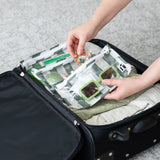 Hands pack sunglasses and a hair clip into Roamio by Bumkins Clear Travel Bag 3 Pack: Clubhouse Stripe in an open suitcase on gray carpet.