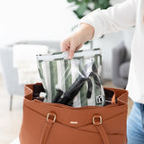 A person places a Roamio by Bumkins Clear Travel Bag 3 Pack: Clubhouse Stripe with a camera tripod in a brown purse.