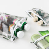Close-up of Roamio by Bumkins Clear Travel Bag 3 Pack: Clubhouse Stripe with vitamins and toiletries on a white background.