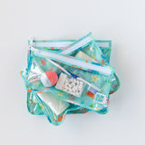 Bumkins Clear Travel Bag 3-Pack: Ocean Life, TSA compliant and reusable, filled with toiletries on a white background.
