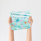 A child holds Bumkins Clear Travel Bag 3-Pack: Ocean Life—reusable, TSA-compliant bags with sea animal designs.