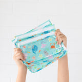 Child holds Bumkins Wet Bag + Clear Travel Bag 3 Pack Set: Ocean Life against a plain white background.