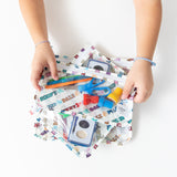 A child holds Bumkins Clear Travel Bag 3 Pack: Mickey & Friends Varsity filled with art supplies at a white table.