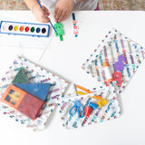 A child paints with watercolors at a table, surrounded by Bumkins Clear Travel Bag 3 Pack: Mickey & Friends Varsity filled with art supplies.