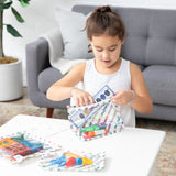 A girl in a white dress packs art supplies into Bumkins Clear Travel Bag 3 Pack: Mickey & Friends Varsity at a table in the living room.