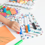 A child's hand reaches for markers from Bumkins Clear Travel Bag 3 Pack: Mickey & Friends Varsity on a table, surrounded by art supplies.