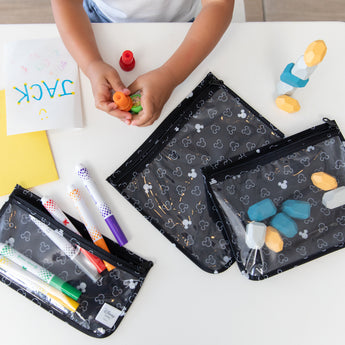 A child plays with markers, stamps, and art supplies in Bumkins Clear Travel Bag 3-Pack: Mickey Mouse Icon Black + White at a white table.