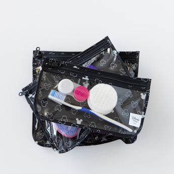 Bumkins Clear Travel Bag 3-Pack: Mickey Mouse Icon Black + White lays stacked on a white background, filled with toiletries.
