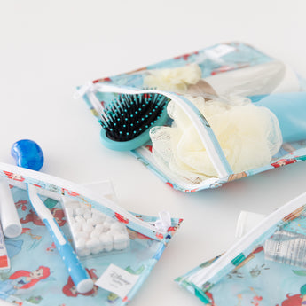Close-up of Bumkins Clear Travel Bag 3 Pack: Disney Princess Ariel filled with toiletries on a white background.