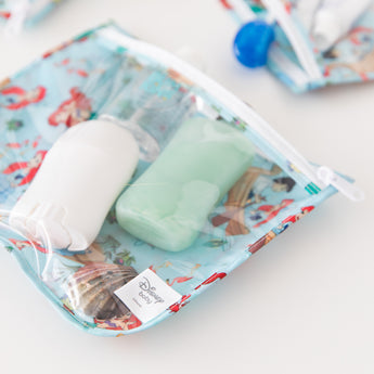 Close-up of Bumkins Clear Travel Bag 3 Pack: Disney Princess Ariel filled with travel-sized bottles on a white background.