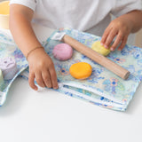 A child wearing a bracelet zips a Bumkins Clear Travel Bag 3 Pack: Aloha Stitch filled with colorful modeling clay on a white table.