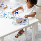 A curly-haired child plays with markers and toys in Bumkins Clear Travel Bag 3 Pack: Aloha Stitch at a white table.