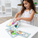 A girl reaches for craft supplies in Bumkins Clear Travel Bag 3 Pack: Aloha Stitch at a white table.