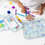 A child uses markers and crafts at a white table, surrounded by Bumkins Clear Travel Bag 3 Pack: Aloha Stitch.