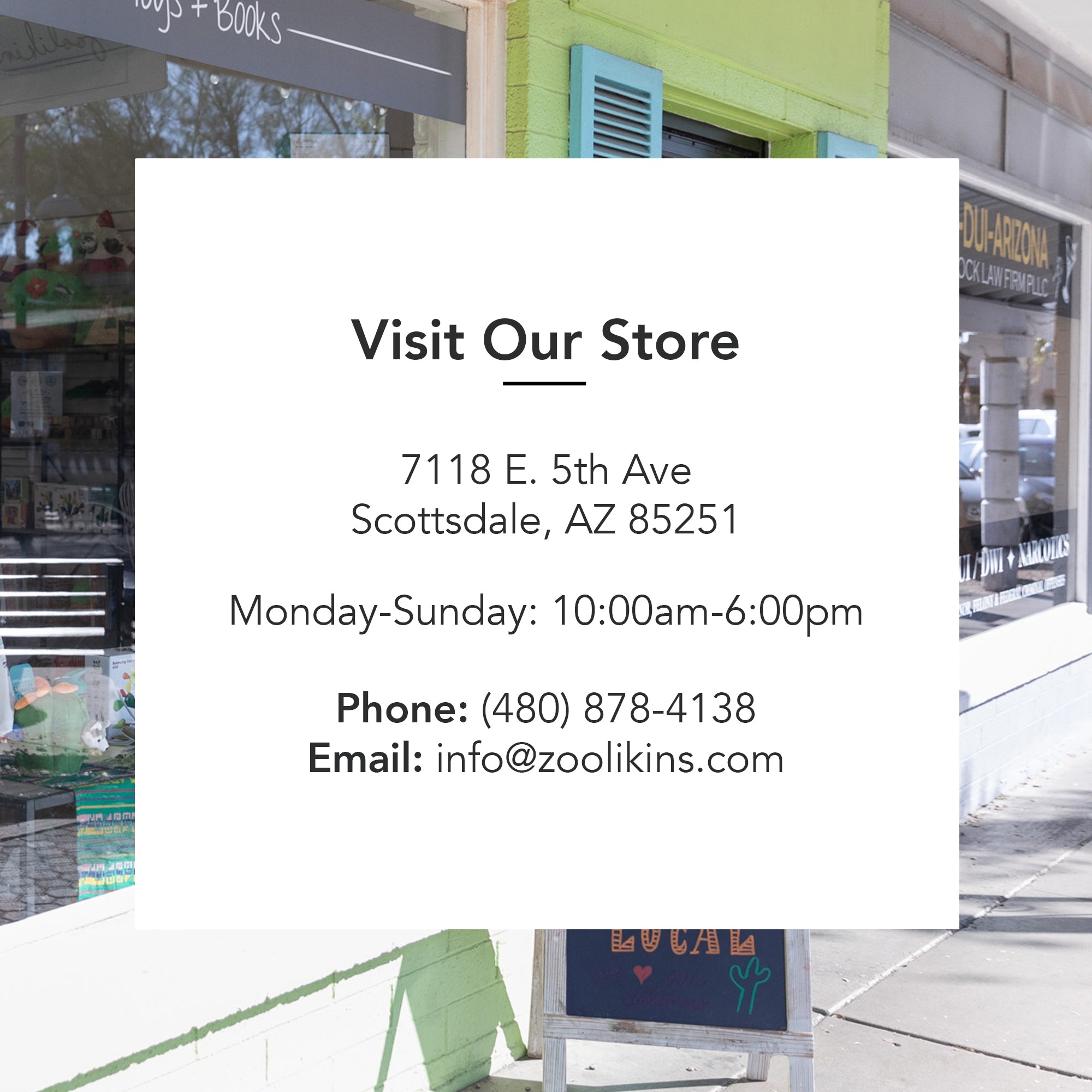 Store window with a sign listing information: Visit Our Store. 7118 E. 5th Ave, Scottsdale, AZ 85251. Monday-Sunday: 10:00am-6:00pm. Phone: (480) 878-4138. Email: info@zoolikins.com. The background shows partial views of the storefront and street.