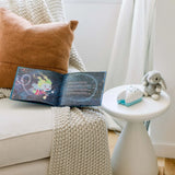 A childrens book, cozy chair, knitted blanket, brown cushion nearby with a plush rabbit and Tooth Fairy Flylight Box Set on a table.