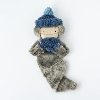 The Holiday Bigfoot Bundle Snuggler by Slumberkins is a whimsical plush with a beige face, blue hat and scarf, and soft gray fur.