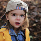 Child in a Storied Hats khaki Lil Hat with organic cotton denim jacket and yellow coat, gazing at the camera against a Southwest backdrop.