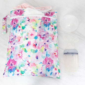 Bumkins Wet/Dry Bag: Watercolor filled with cloth diapers, placed next to a breast pump on a white marble surface.