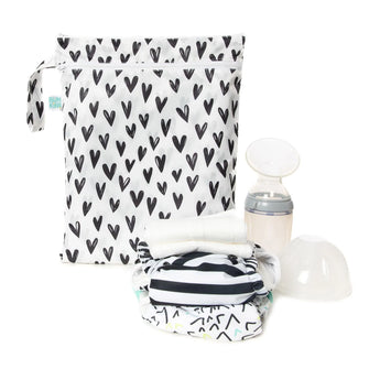 A breast pump and a stack of cloth diapers sit in front of Bumkins Wet/Dry Bag: Hearts on a white background.
