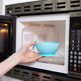 A person places a Bumkins Silicone First Feeding Set: Blue into an open microwave.