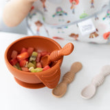 Close-up of Bumkins Silicone First Feeding Set: Clay with diced fruit on a high chair tray next to two baby spoons.