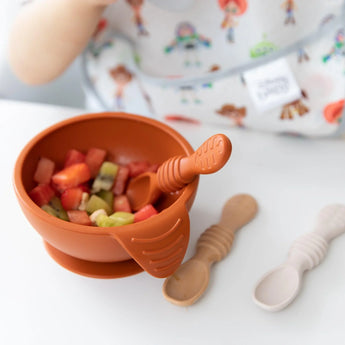 Close-up of Bumkins Silicone First Feeding Set: Clay with diced fruit on a high chair tray next to two baby spoons.