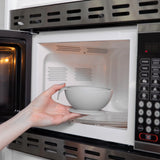 A person places a Bumkins Silicone First Feeding Set: Gray into an open microwave.