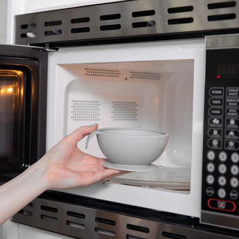 A person places a Bumkins Silicone First Feeding Set: Gray into an open microwave.