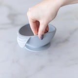 A hand holds a Bumkins Silicone First Feeding Set: Gray, demonstrating the suction cup bottom on a marble surface.
