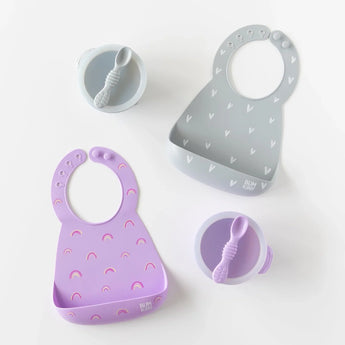 Bumkins Silicone First Feeding Set: Lavender, a gray bowl & spoon, and two gray and purple silicone bibs are arranged on a white background.