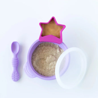 Bumkins Silicone First Feeding Set: Lavender with oatmeal and a pink star-shaped cup of peanut butter sit on a white background.