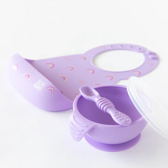 Bumkins Silicone First Feeding Set: Lavender sits on a white background with a matching silicone bib blurred behind.