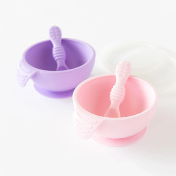 Bumkins Silicone First Feeding Set: Pink sits in front of a purple bowl and spoon set on a white background.