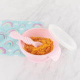 Bumkins Silicone First Feeding Set: Pink with orange mash on a marble surface next to a rainbow print pouch.