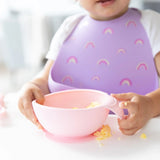 Close-up of a child in a purple silicone bib holding a bowl with eggs from Bumkins Silicone First Feeding Set: Pink.