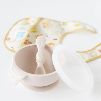 Bumkins Silicone First Feeding Set: Sand sits on a white background, with a colorful bib blurred behind.