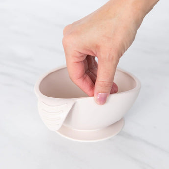 A hand holds a Bumkins Silicone First Feeding Set: Sand, demonstrating the suction cup bottom on a marble surface.